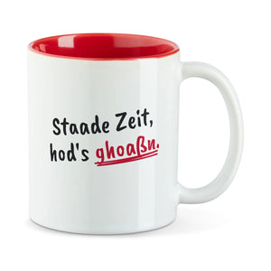 Weiße Tasse mit roter Innenseite und dem bairischen Spruch „Staade Zeit, hod's ghoaßn.“ in Pinselschrift.