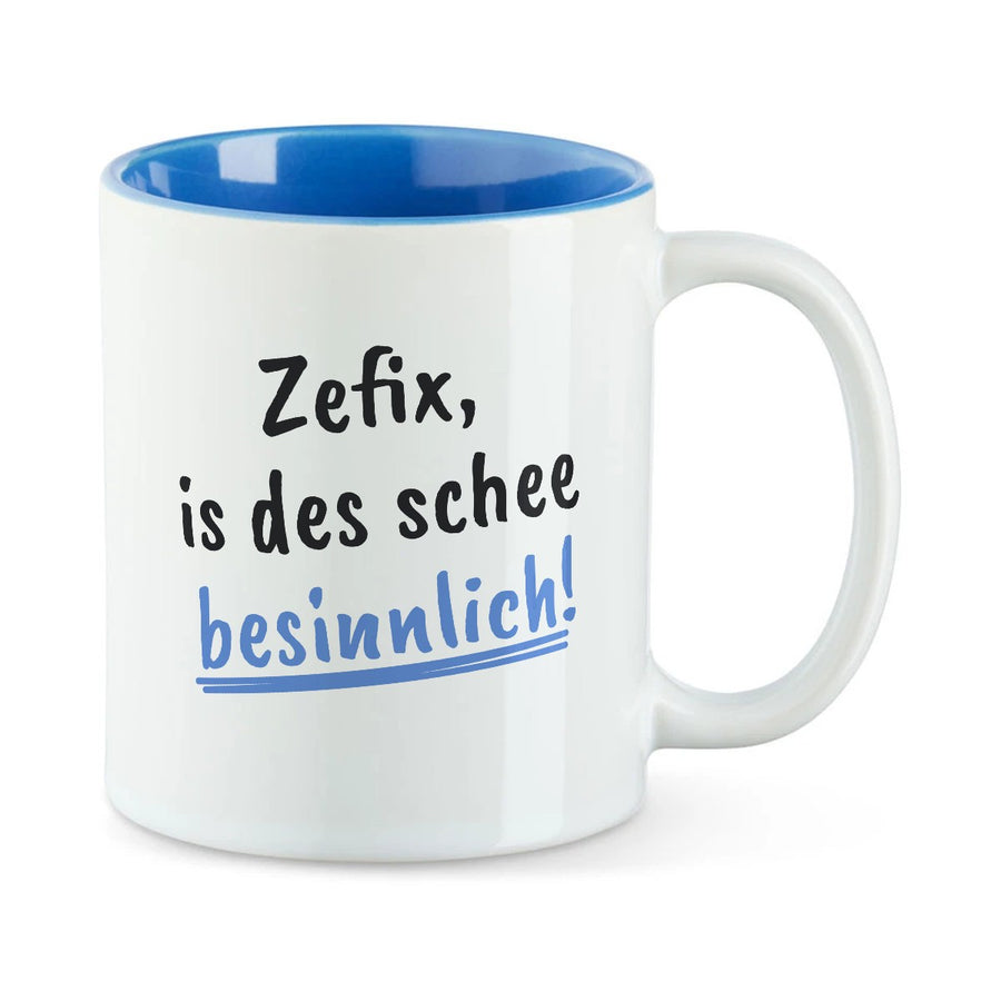 Weiße Tasse mit blauer Innenseite und dem bairischen Spruch „Zefix, is des schee besinnlich!“ in Pinselschrift.