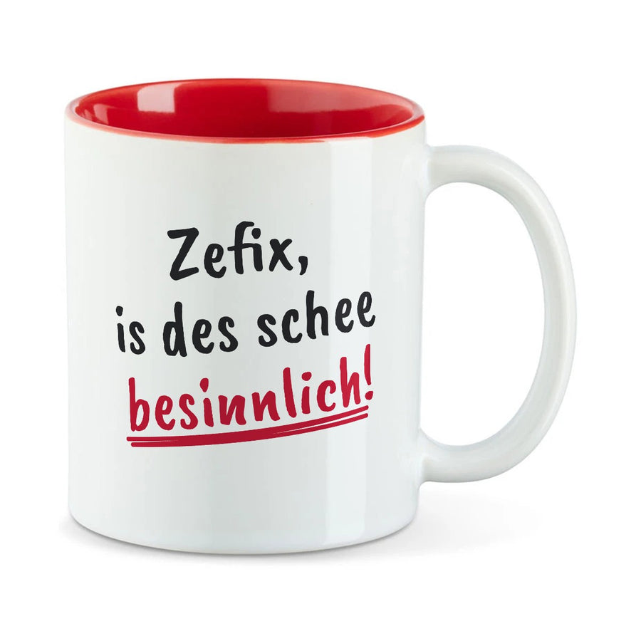 Weiße Tasse mit roter Innenseite und dem bairischen Spruch „Zefix, is des schee besinnlich!“ in Pinselschrift.